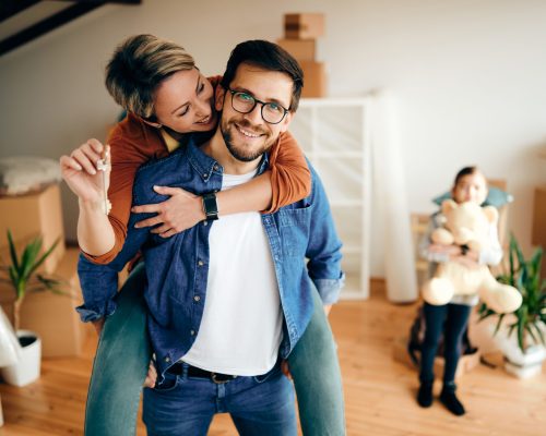 Happy mid adult couple having fun while relocating into a new house. Their daughter is in the background.